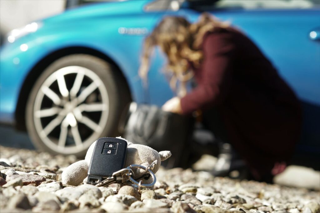 Autoschlüssel auf Kies vor einem Auto mit unscharfer Person im Hintergrund, symbolisiert den Verlust von VW Schlüsseln und die Suche nach Lösungen.