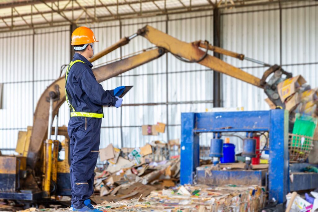 Ein Mitarbeiter in Schutzkleidung überwacht den Recyclingprozess in einer Industrieanlage, unterstützt durch moderne Wertstoffsammler zur effizienten Mülltrennung.