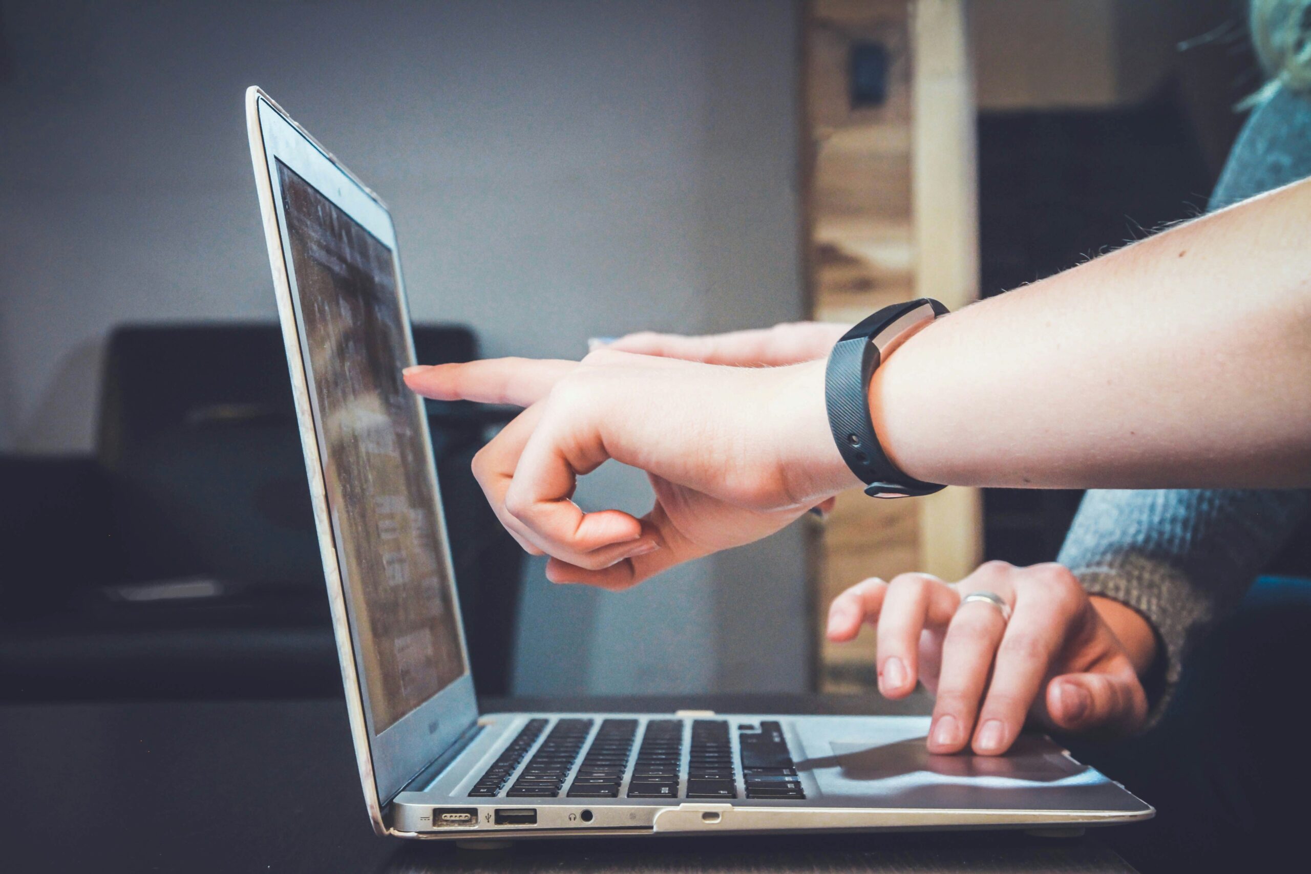 Zwei Personen arbeiten an einem Laptop. Eine Person zeigt mit ihrem Finger auf den Bildschirm 