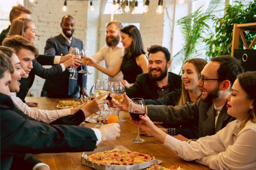 Mitarbeiter genießen eine entspannte Betriebsfeier NRW mit Pizza, Wein und festlicher Stimmung in einem gemütlichen Restaurant.