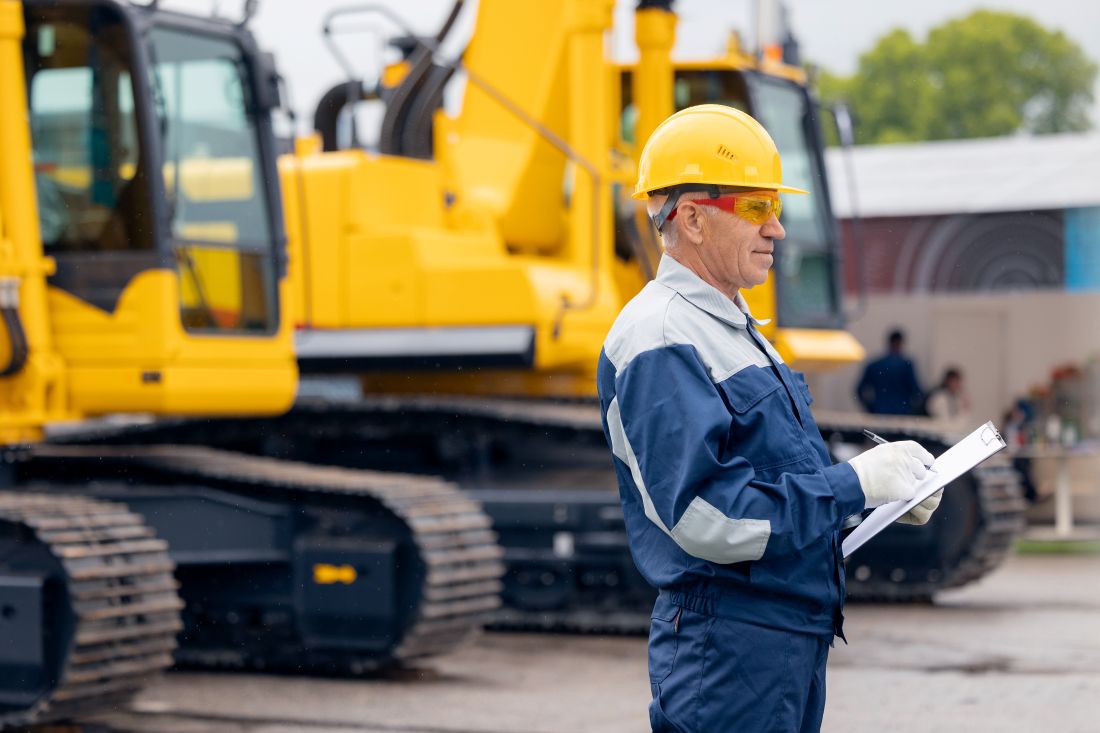 Bauleiter kontrolliert Baustelle mit gelben Baggern im Hintergrund