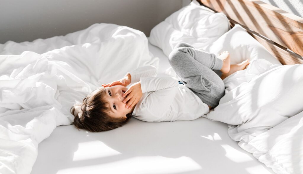 Kind liegt entspannt auf heller Bettwäsche – visuelle Darstellung für Alltagsszenen mit Matratzenschutz im Familienhaushalt