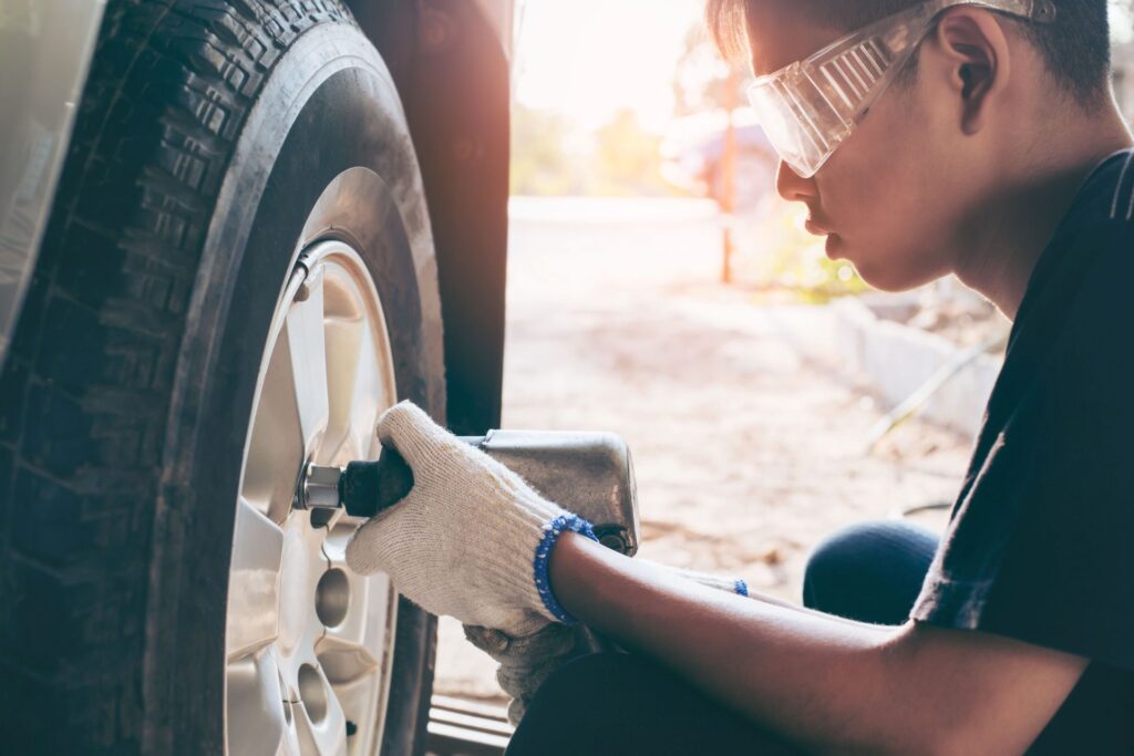 Mechaniker mit Schutzbrille nutzt ein Druckluftwerkzeug zur Reifenmontage an einem Auto